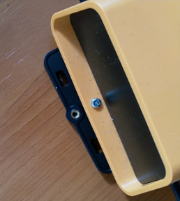 Small screw being inserted through hole at top of yellow device into mounting bracket.