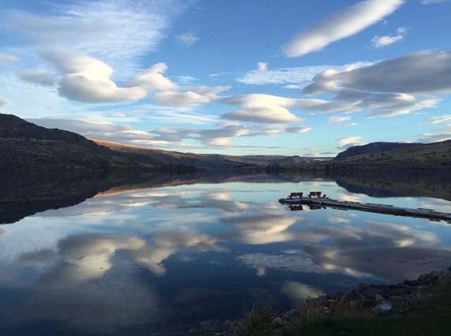 Lago que refleja montañas y nubes en aguas tranquilas al atardecer o al amanecer.