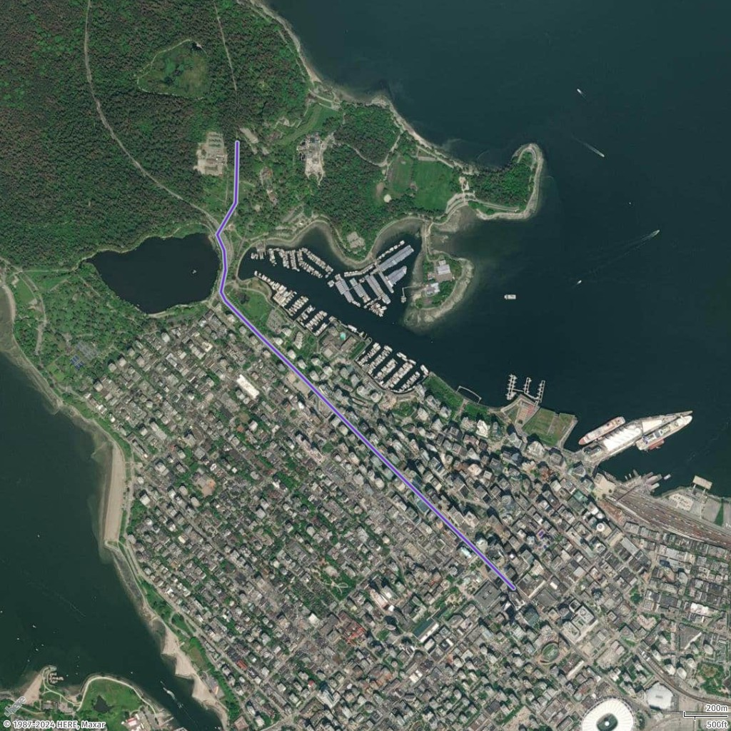 Aerial view of coastal city with dense urban area, marina, and surrounding forests.