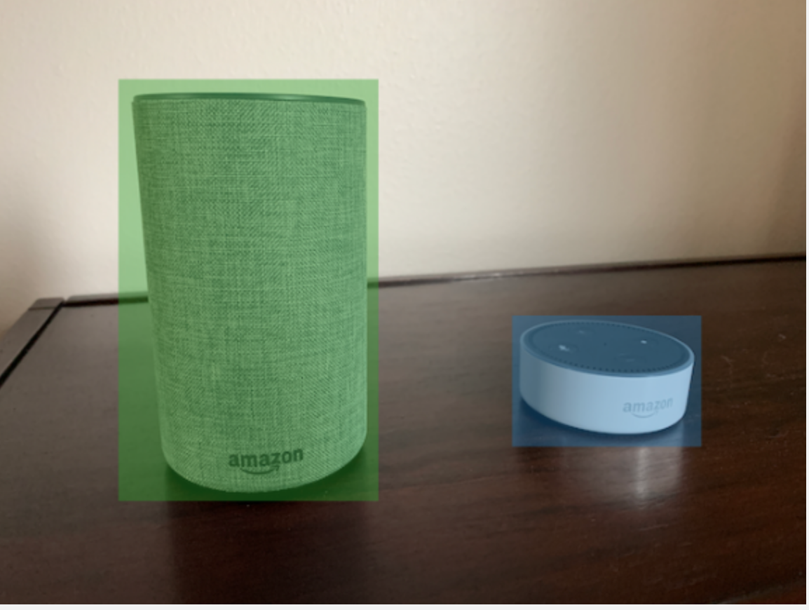 Two Amazon smart speakers, one with green bounding box and one blue bounding box, on a wooden surface.