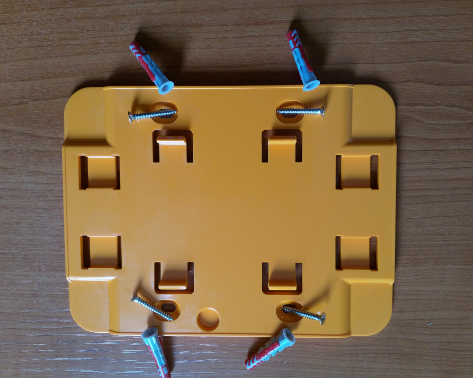 Yellow plastic mounting bracket with screw holes and wall anchors for installation.